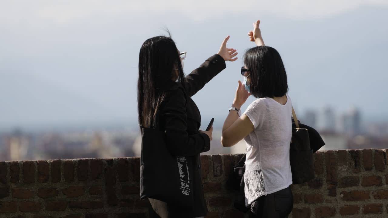 흐릿한 경치를 배경으로 사진 촬영을 위해 친구를 안내하는 여성 관광객