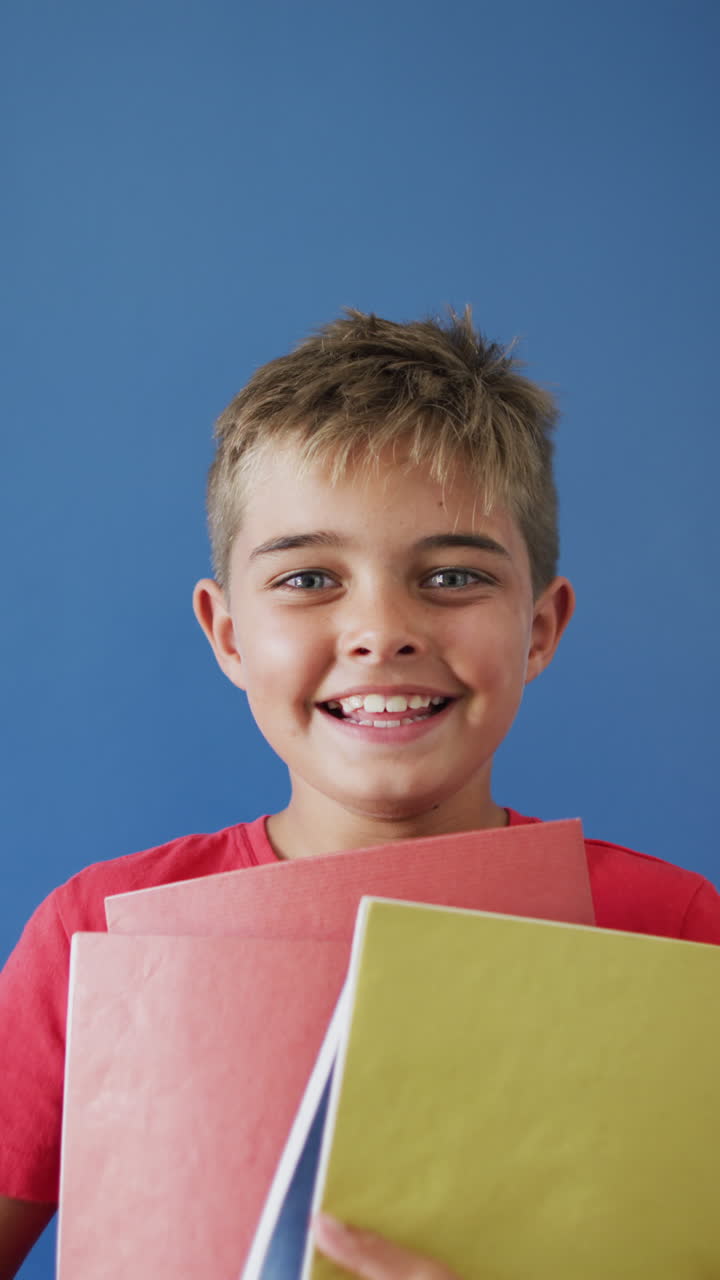 Vertikales Video eines glücklichen Jungen, der Bücher vor blauem Hintergrund hält, mit Platz für Text, in Zeitlupe