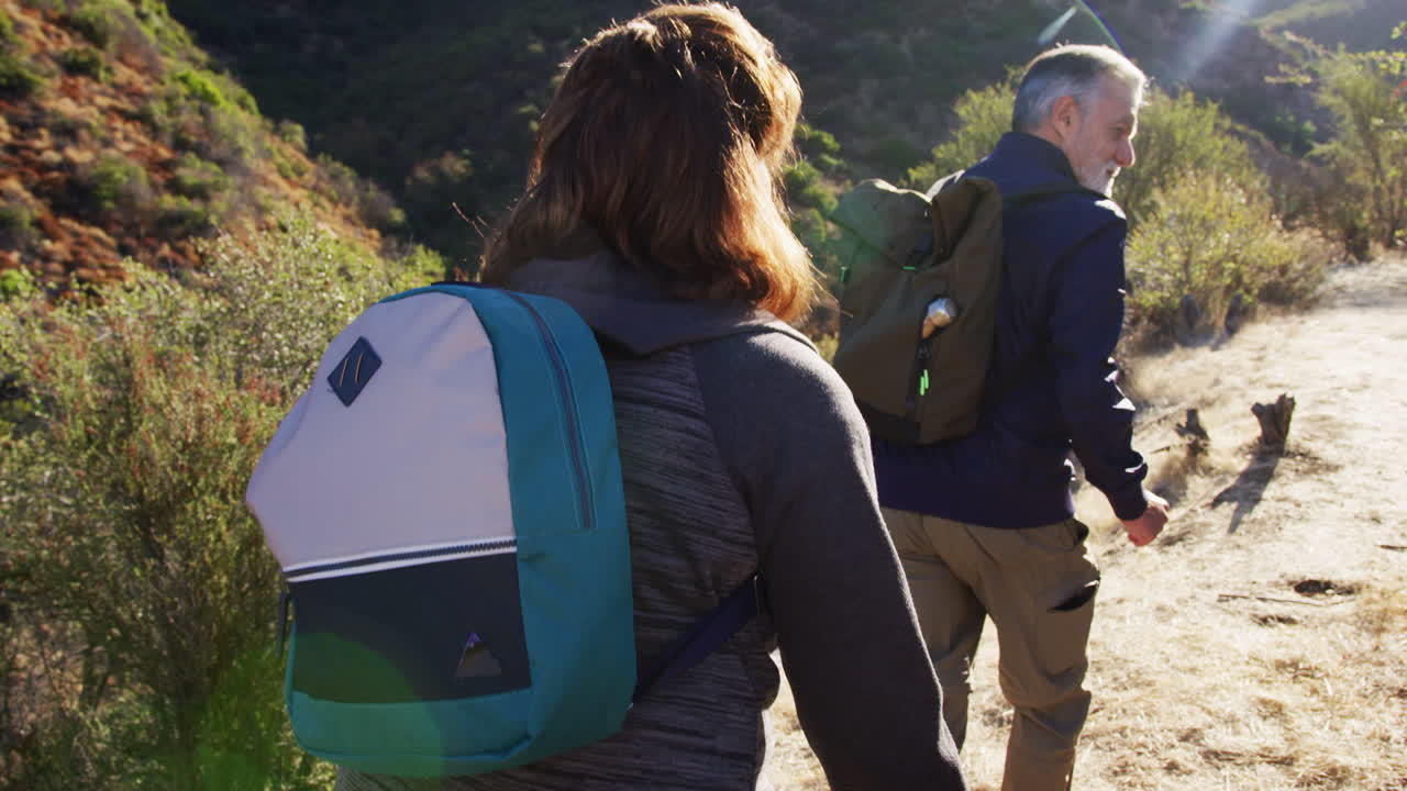 vista posterior de un grupo de amigos mayores que van de excursión a lo largo del sendero en el campo juntos