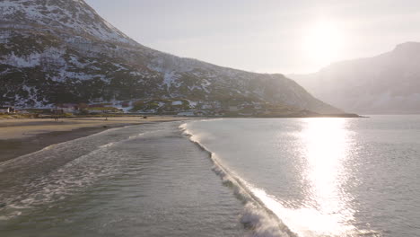 Pequeñas-Olas-Corren-Hacia-La-Playa-ártica-De-Arena,-Nieve-Irregular-En-La-Montaña