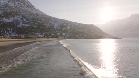 pequeñas olas corren hacia la playa ártica de arena, nieve irregular en la montaña