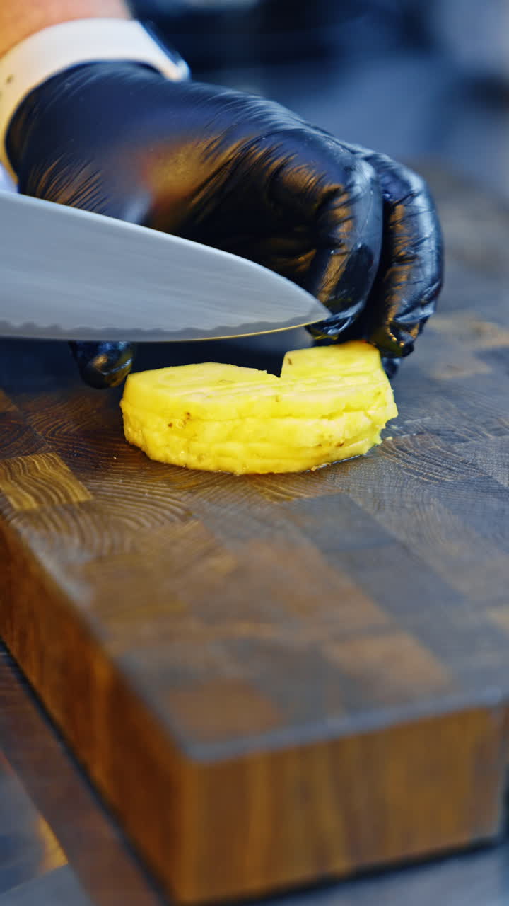 A cook carefully cuts the pineapple half-rings. Chef preparing food in the restaurant. Close up. Vertical video.
