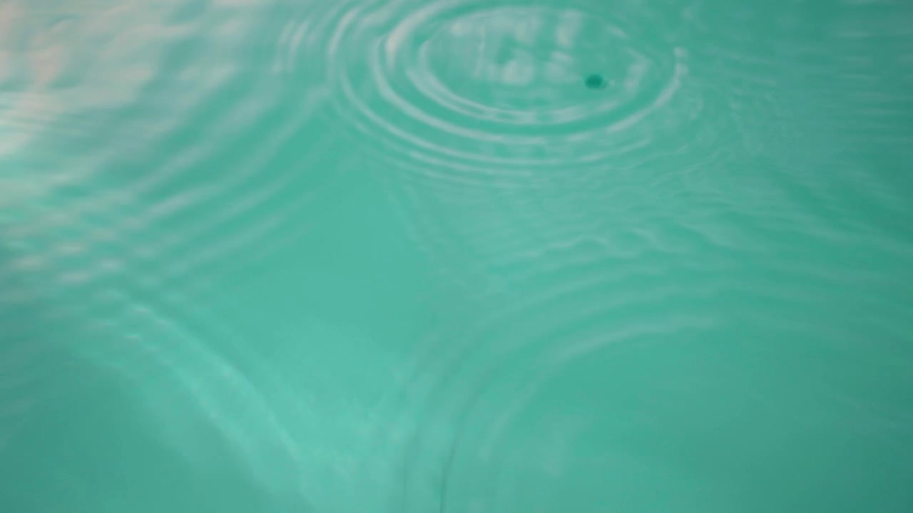 Ripresa dall'alto al rallentatore di singole gocce di pioggia che cadono su una superficie d'acqua calma, creando onde e increspature