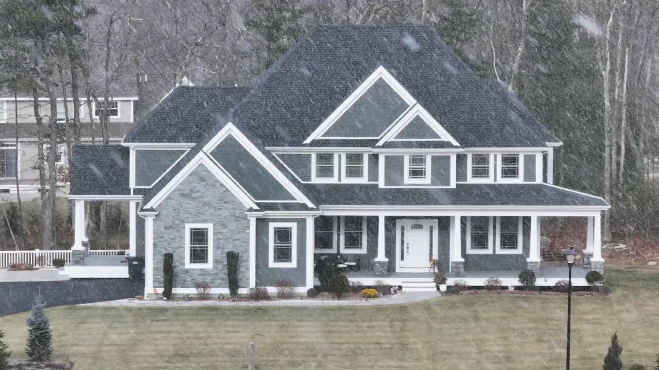 Snowstorm in american Suburb district with large single family homes. Aerial zoom shot. Snowy winter day in rural area. Luxury mansion with Black roof and large garden.