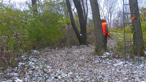 cazador vestido de naranja y camuflaje caminando por un sendero de caza a principios del medio oeste americano