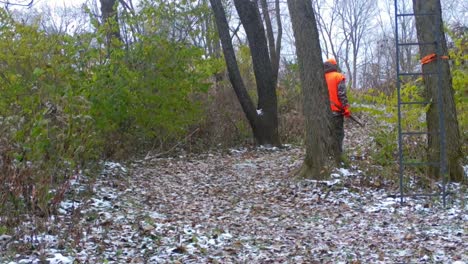 hunter dressed in orange and camouflage walking along a game trail in early inter in american midwest