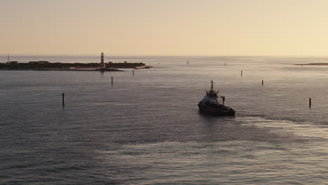 tugboat navigating a harbor channel at sunset/sunrise