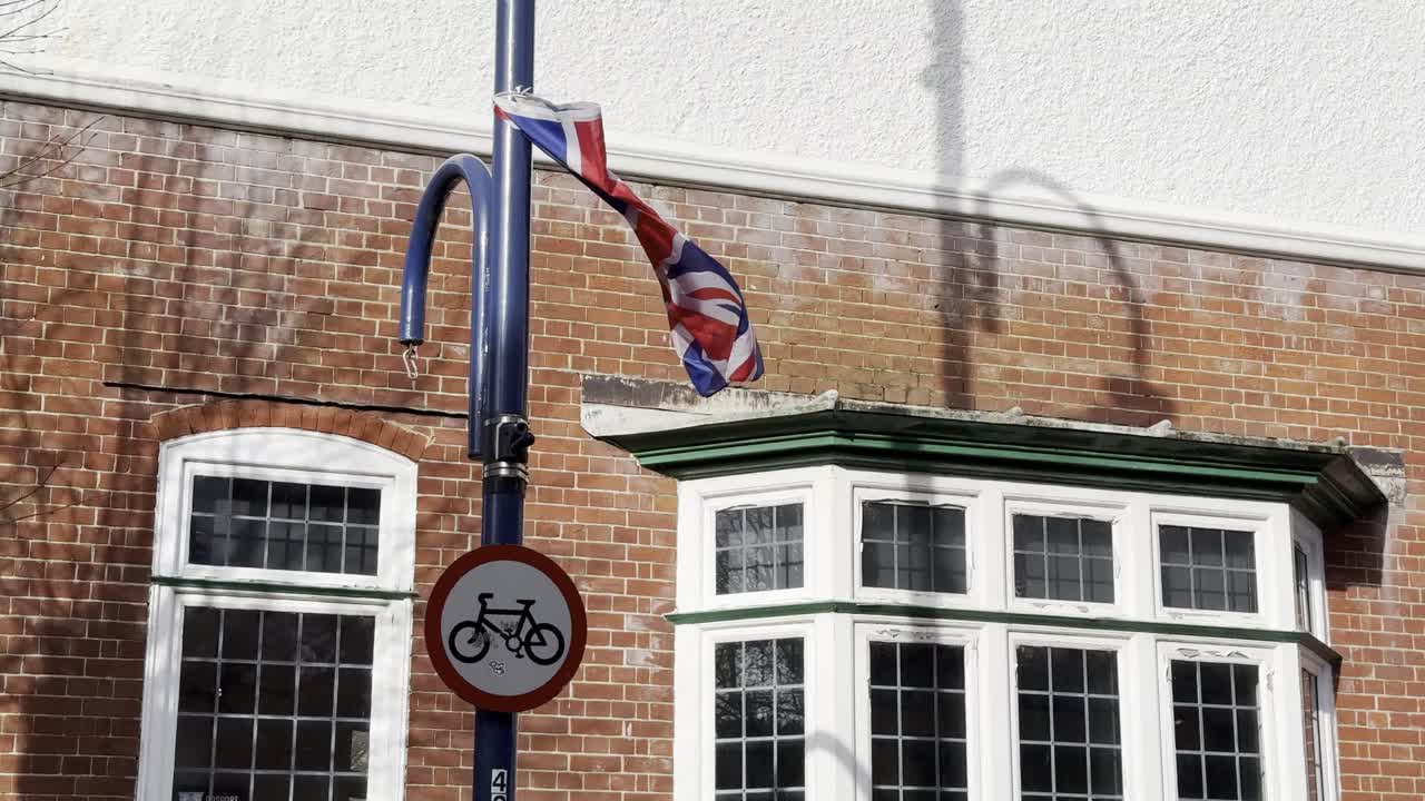 Union Jack -lippu liehuu katupylväässä tiilirakennusta vasten.