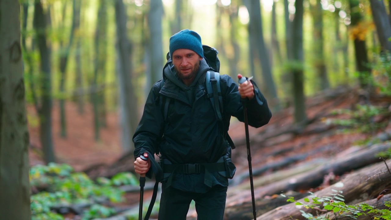 Focused Man with Backpack and Trekking Poles Hiking in Forest