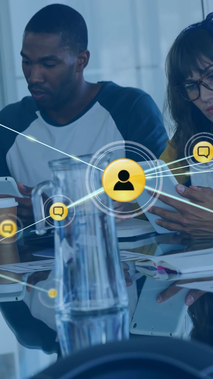 Vertical video: Team tapping tablets at desk making user or chat icons over glass forming tech netwo