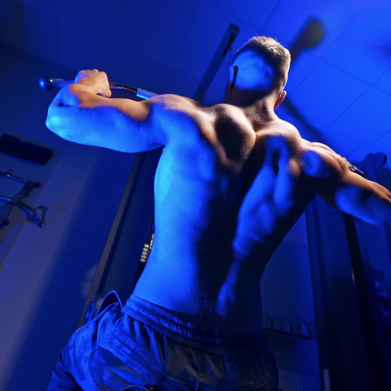 Brutal strong athletic men pumping up muscles. Doing workout on sport equipment - muscular bodybuilder doing exercises in gym with naked torso. Fitness and bodybuilding concept. Video from the back.