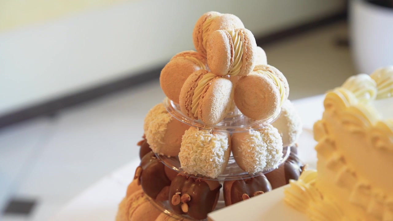 Uno scatto ravvicinato dettagliato di una torre di macaron e pasticcini a più livelli elegantemente esposta su un tavolo da dessert, con tonalità cremose, texture delicate e illuminazione naturale soffusa per un'atmosfera raffinata