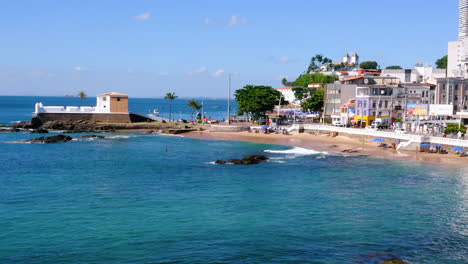 Aerial-view-of-Santa-Maria-Fort,-the-beach,-the-neighborhood,-some-boats-parked-and-the-Farol-da-Barra-at-background,-Salvador,-Bahia,-Brazil