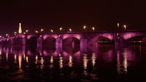 un histórico puente de piedra iluminado en rosa sobre aguas tranquilas por la noche en blois, francia