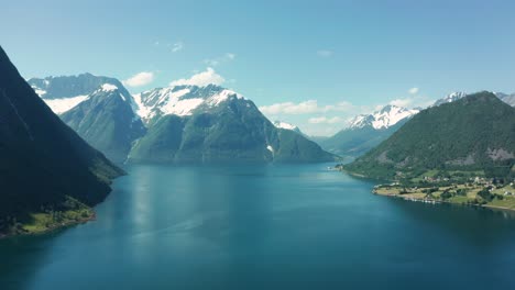 vista aérea de un fiordo azul profundo rodeado de altos acantilados y montañas en noruega, bajo un cielo brillante con la comunidad costera en el borde