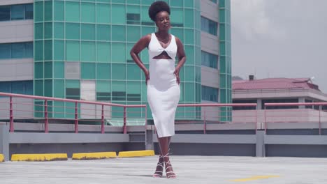 with the city skyline in view, a black girl in a white dress stands on a rooftop