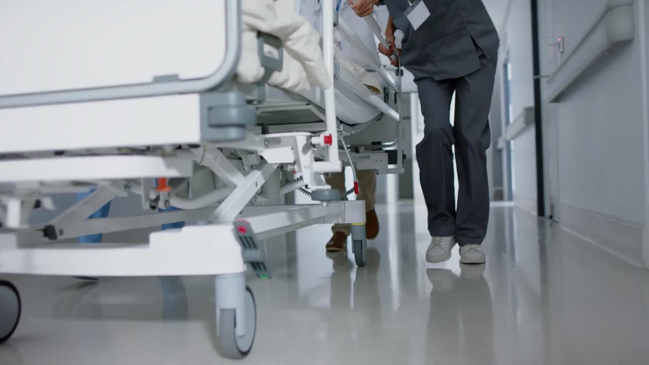 Medici e chirurghi di diverse etnie che camminano con un paziente su un letto d'ospedale, al rallentatore.