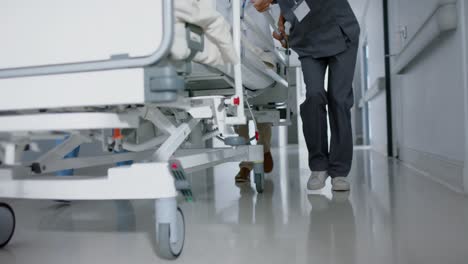 Diverse-doctor-and-surgeons-walking-with-patient-on-hospital-bed-in-slow-motion