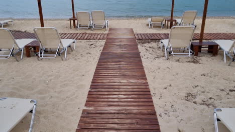 Tilt-up-view-between-wooden-parasols-and-empty-sunbeds-on-a-sandy-beach