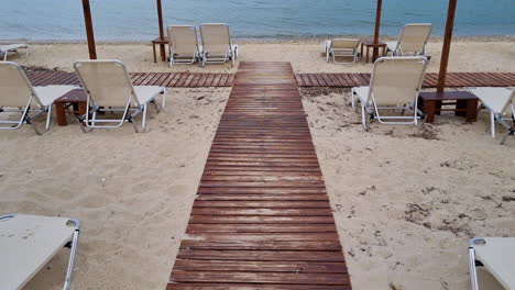 vista inclinada entre sombrillas de madera y tumbonas vacías en una playa de arena