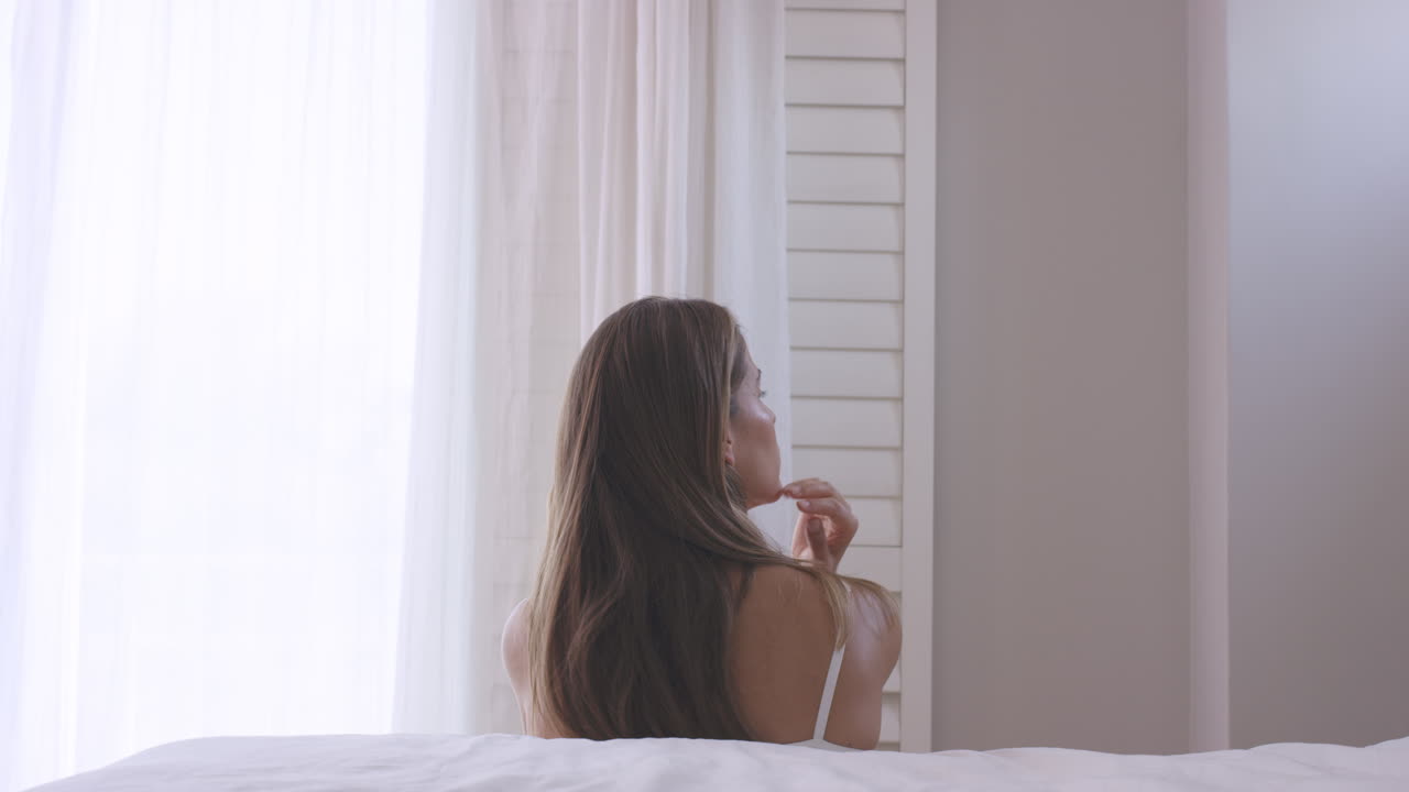 슬픈 젊은 여성이 속옷을 입고 창문 밖을 보고 있습니다.