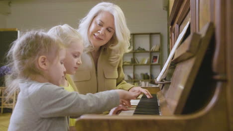 two little girls playing old piano at home while their grandmother watching them 1