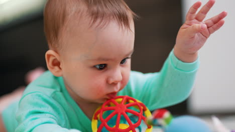 baby boy lies on belly with his face to the camera. close up. adorable kid interested in a bright toy. blurred backdrop.