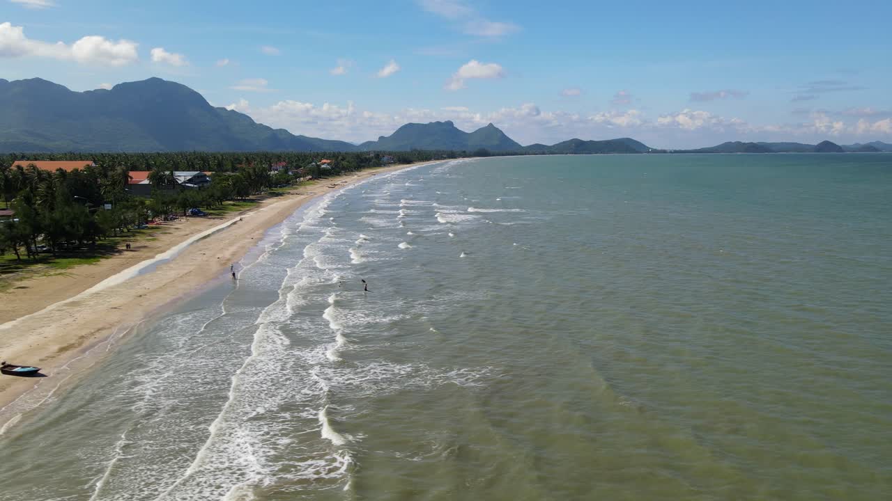 Toma aérea deslizándose hacia la izquierda que revela un barco de pesca, personas en el agua y un paisaje magnífico.