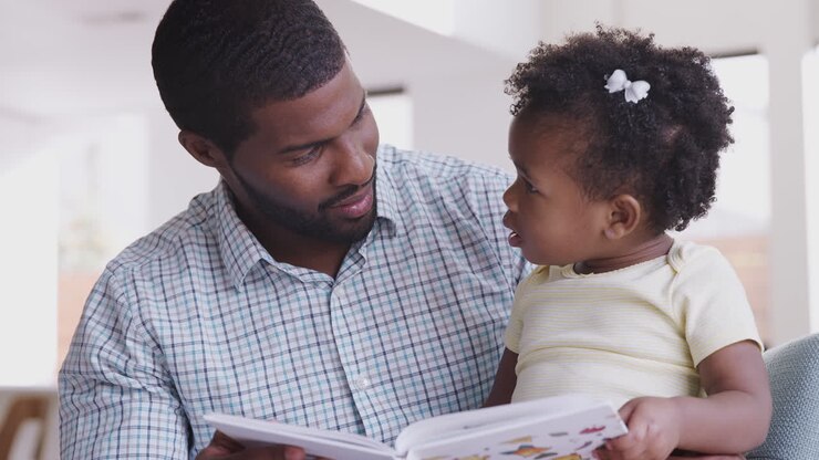 Figlia piccola e padre seduti sul divano che leggono un libro insieme.