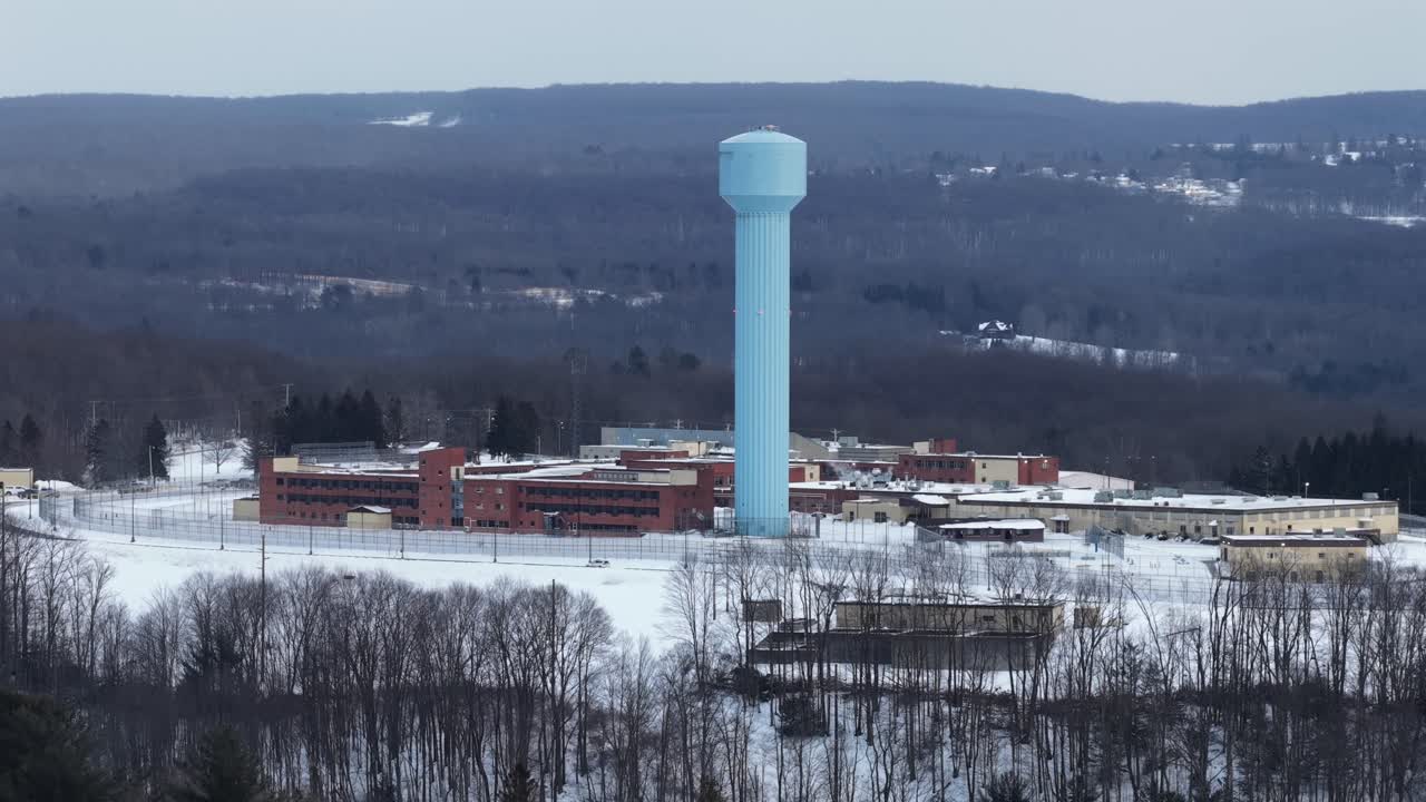 Veduta aerea di una struttura penitenziaria a Loretto, Pennsylvania, circondata da terreni innevati e colline boscose, con un'alta torre dell'acqua blu che si erge sopra il complesso. Inquadratura in avvicinamento. Pennsylvania, USA.