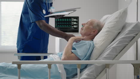 a black male doctor in a protective mask comes in and talks to patients with an elderly white man lying on a hospital bed