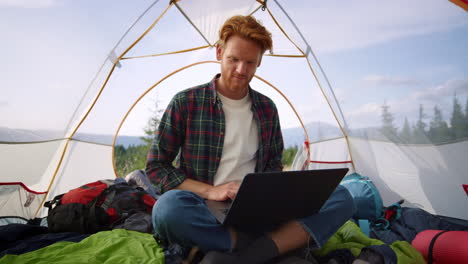 man sitting in camping tent with laptop