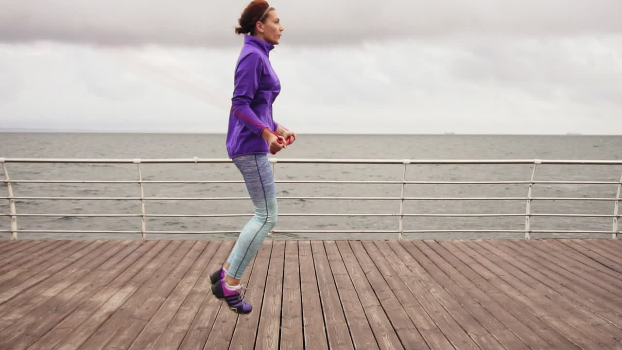 Slow Motion shot of and athletic woman working out on the jump rope. Outdoor sports. Girl jumping on a skipping rope by the sea