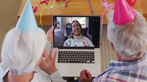 caucasian senior couple on laptop video chat wearing party hats at home