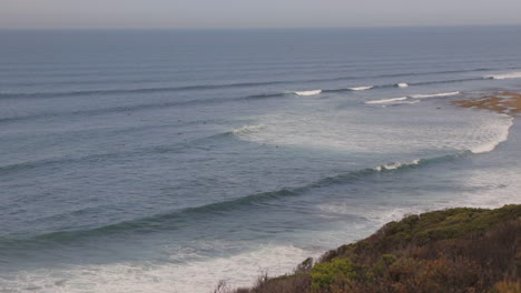 Surfers-in-ocean-at-Bells-Beach-with-big-waves,-day-time,-Australia-Victoria