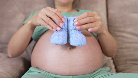 belly of a pregnant girl. future mother playing with knitted baby socks on her bare stomach. concept of health during pregnancy. close-up.