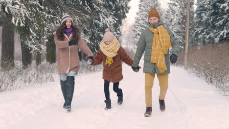 parents and daughter dressed in winter clothes walking in snowy forest