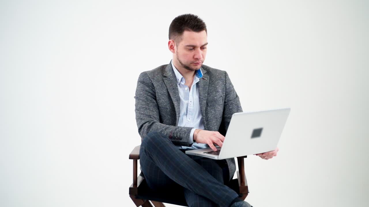 Portrait of serious businessman with a laptop. Thoughtful young man sitting in a chair and working a laptop isolated on white background.