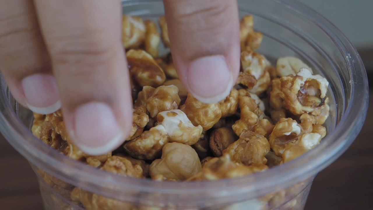 recogiendo a mano palomitas de maíz de caramelo de un recipiente