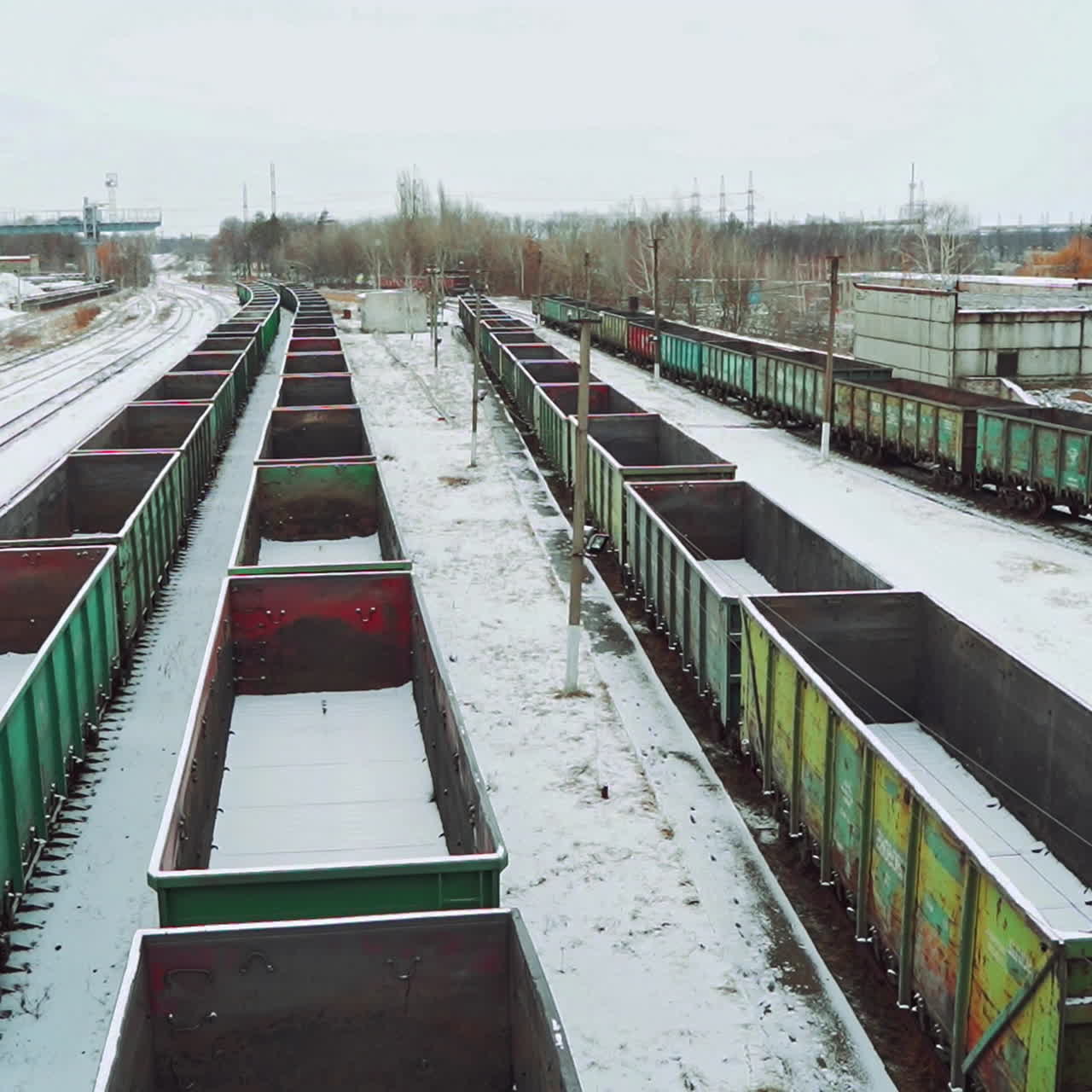 Empty shipping containers are located at an abandoned railway station in the countryside against the background of snow and forest. Aerial view.