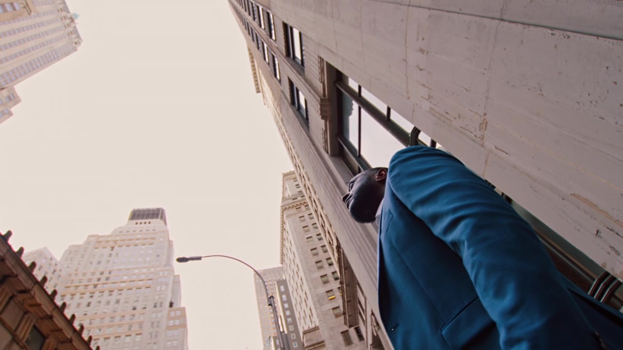 Nueva York, EE. UU., 21 de mayo de 2023: Hombre con Traje Azul Visto desde Abajo entre Rascacielos Urbanos. Un hombre con un blazer azul verdoso se asoma por una barandilla de hierro, visto desde abajo.