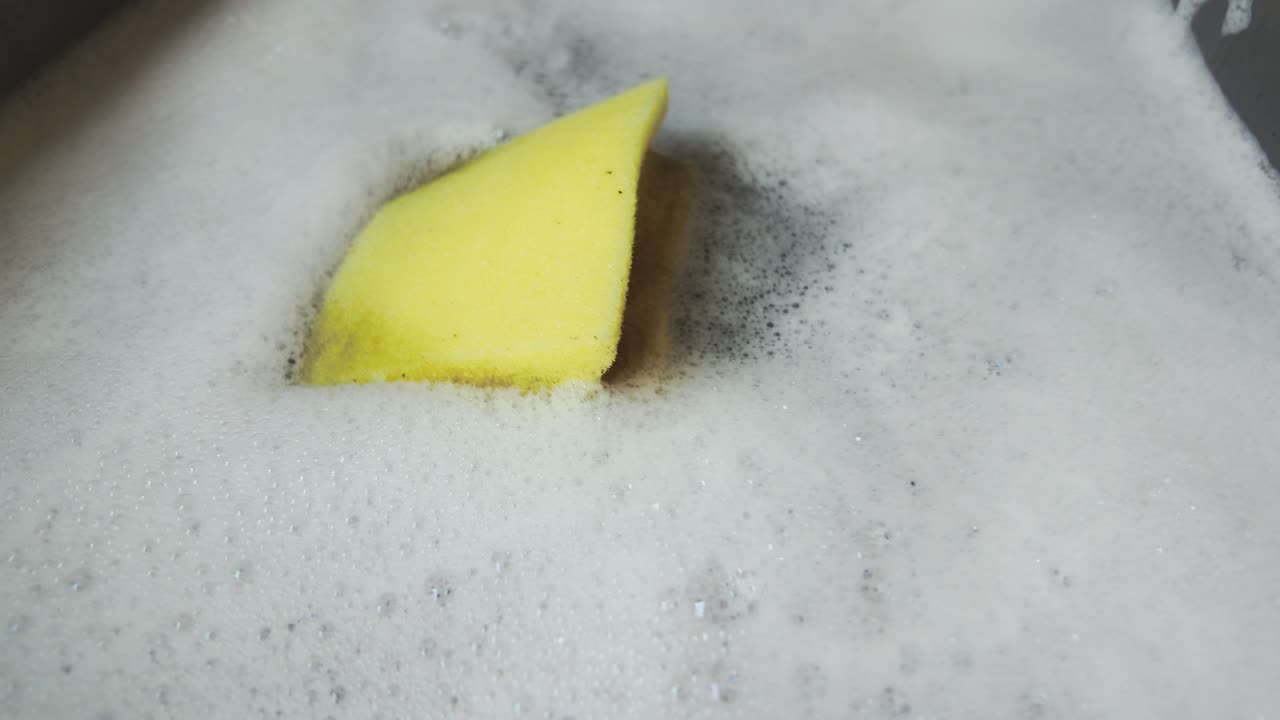 Yellow Dish Washing Sponge floating in foamy soapy water bubbles