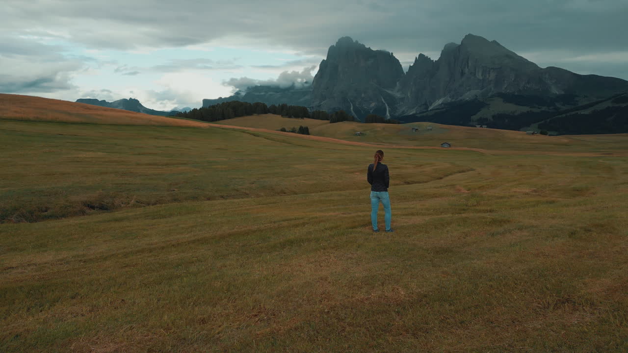 Woman standing in a field admiring the majestic peaks of the Dolomites in Alpe di Siusi, Italy
