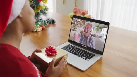 Mujer-Afroamericana-Con-Gorro-De-Papá-Noel-Usando-Una-Computadora-Portátil-Para-Una-Videollamada-Navideña,-Con-Un-Hombre-En-La-Pantalla