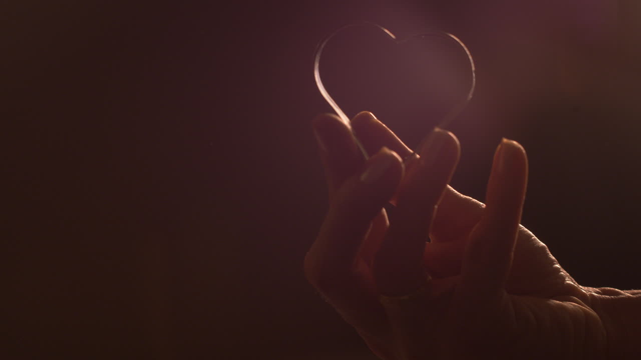 Close up, woman's hand holding heart shaped metal cookie cutter. Ambient light