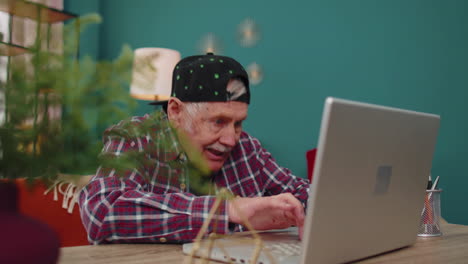 Grandfather-man-playing-computer-video-games-on-laptop-computer,-wins,-celebrate,-smiles-happily