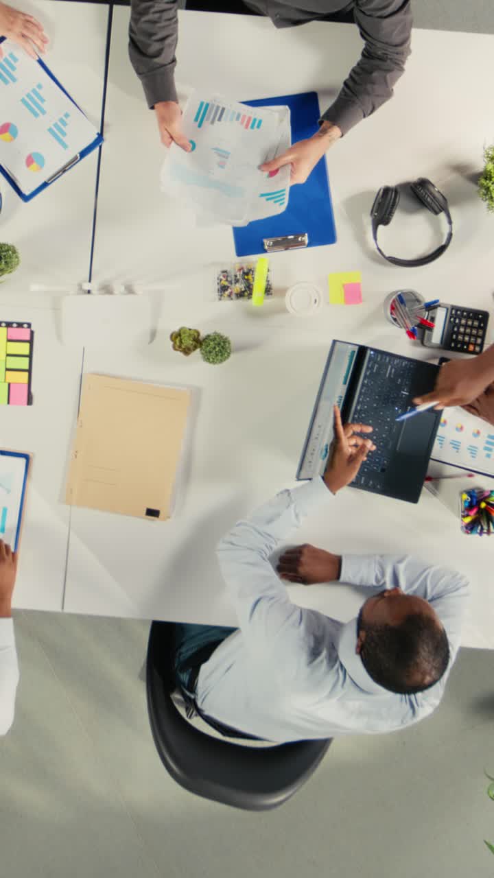 Vertical Video Top down view zoom out of diverse coworkers in meeting discuss budgeting