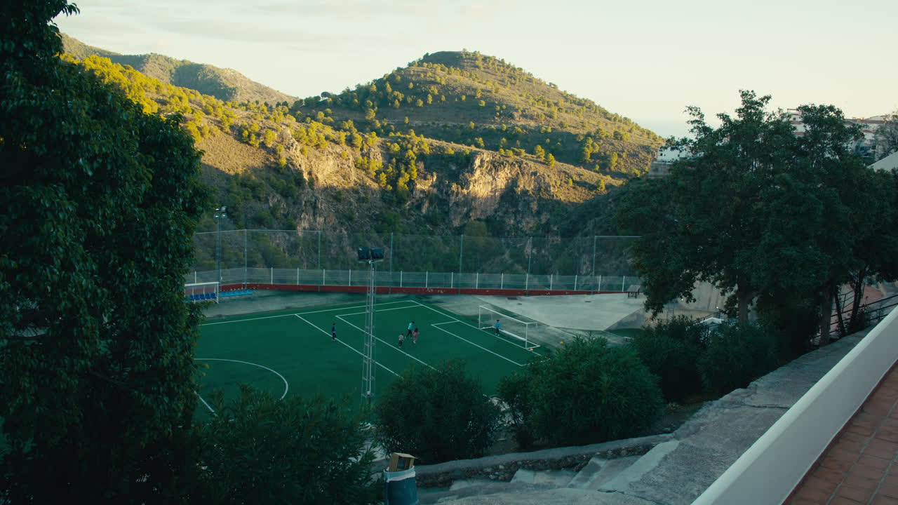 Children play football on a spectacular mountaintop field in southern Spain, surrounded by dramatic Andalusian cliffs and trees