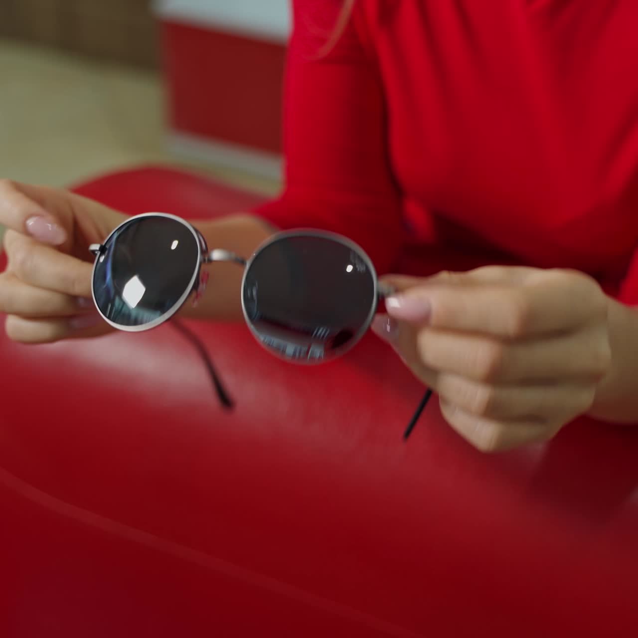 Stylish sunglasses in woman's hands. Girl sits in armchair and holds new trendy black glasses. Close-up. Eyesight concept.
