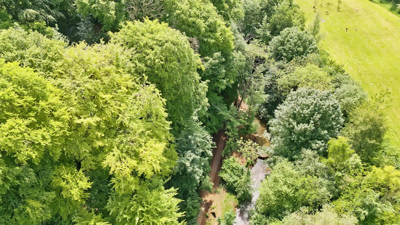 Aerial drone scene of a UK summer park&mdash;people delighting in a meandering stream, inviting picnic areas, and wooded tourist site